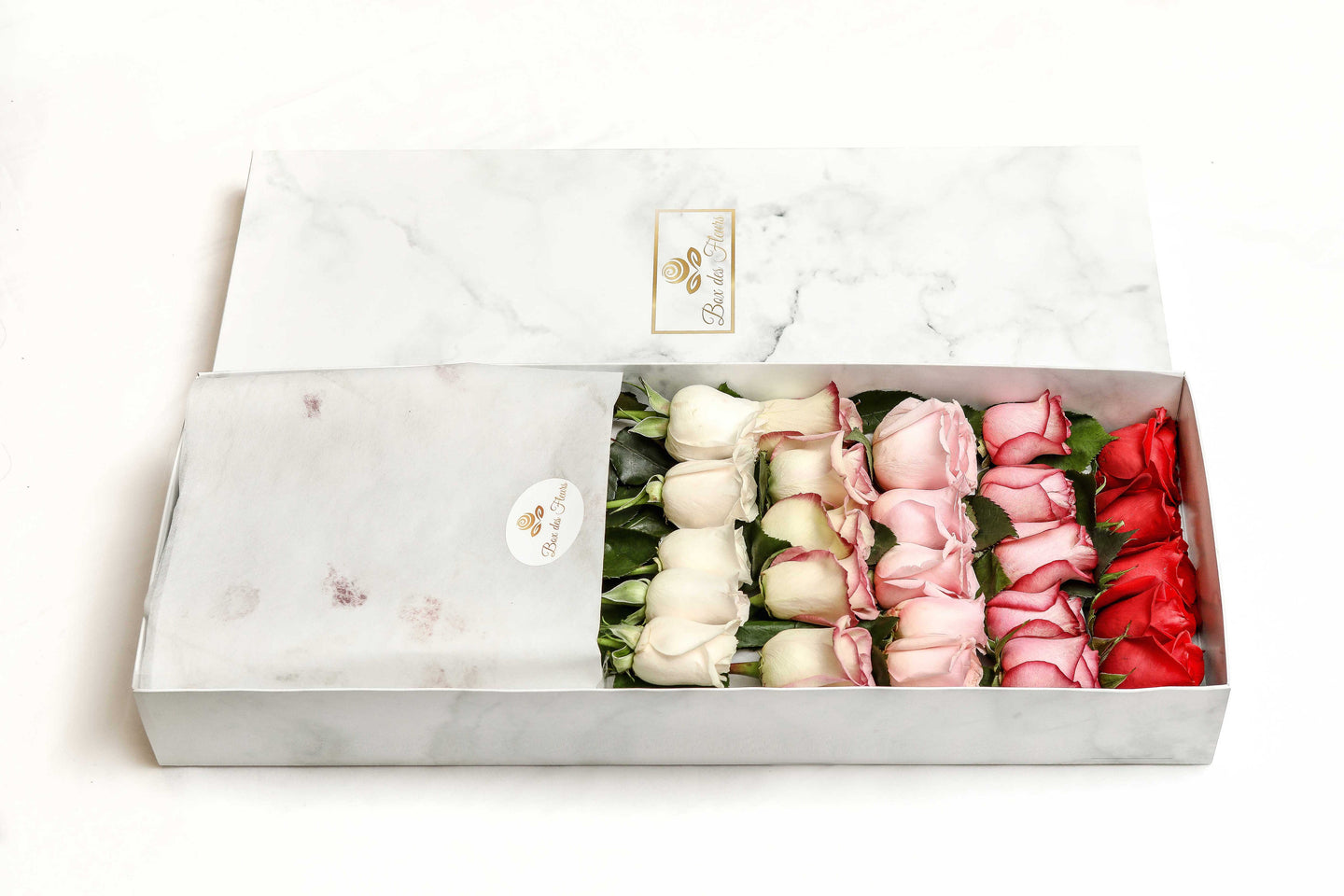 A close-up image of a flower arrangement by Vancouver's Box des Fleurs. The arrangement features 25 different roses in various shades of white, yellow, pink, magenta, and red arranged in an ombre effect inside a white marble box. Perfect for any occasion, order now for fresh, handcrafted flowers from Vancouver's premier florist.