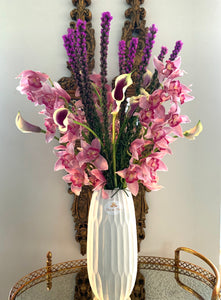 A close-up image of a flower arrangement from Vancouver's Box Des Fleurs, called "Jardin de Papillons" (Butterfly Garden). The arrangement features pink, white, purple, yellow, and green seasonally available flowers, including orchids and other delicate blooms, and green leaves in a round glass vase. Two butterfly-shaped ornaments are perched on branches inside the vase, adding a whimsical touch. Perfect as a gift or to brighten up any room.