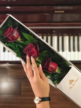 A close-up image of a flower arrangement from Vancouver's Box Des Fleurs, called "Mousquetaire" (Three Musketeers). The arrangement features three long-stemmed red roses in a triangular shape with lush green leaves in a white marble box. The minimalist and elegant design of the arrangement makes it perfect for any occasion, from romantic gestures to expressing appreciation.