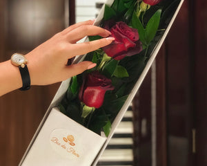 Mousquetaire" (Three Musketeers). The arrangement features three long-stemmed red roses in a triangular shape with lush green leaves in a white marble box. The minimalist and elegant design of the arrangement makes it perfect for any occasion, from romantic gestures to expressing appreciation.